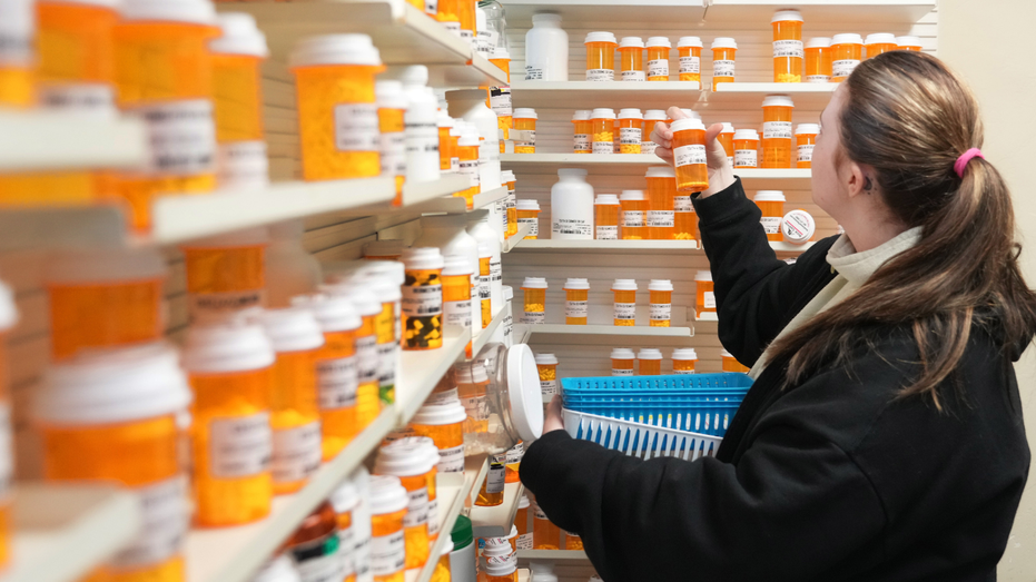 Un technicien en pharmacie sort des médicaments d'une étagère à l'intérieur d'une pharmacie