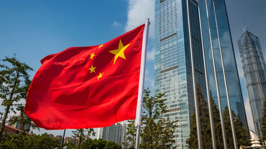 Le champ rouge vif et les étoiles jaunes du drapeau de la République populaire de Chine volent dans la brise à côté des tours futuristes de verre et d'acier des gratte-ciel de Pudong, à Shanghai, en Chine.