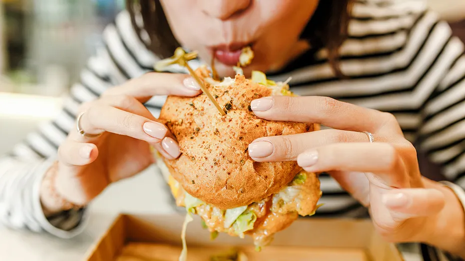 Femme mangeant un hamburger dans un café fastfood moderne, concept de déjeuner