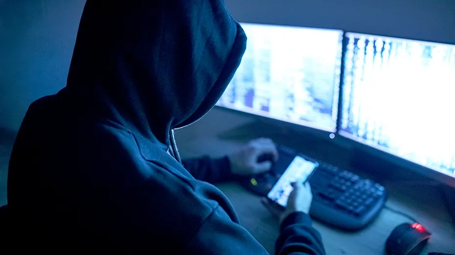 Un pirate informatique utilisant un téléphone et un ordinateur.