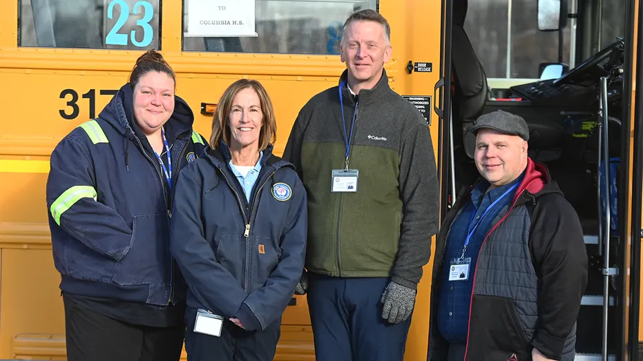 Kurtis Kotes se tient avec le personnel du transport scolaire devant un autobus scolaire jaune.