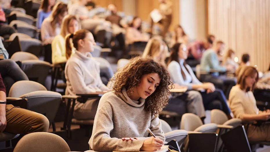 Les étudiants sont assis dans une salle de conférence pendant qu'un étudiant prend des notes pendant les cours.