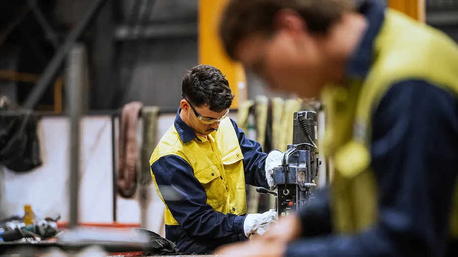 Soudeurs qualifiés travaillant sur la construction en acier, le meulage et le soudage de pièces en fer dans un entrepôt moderne et lumineux