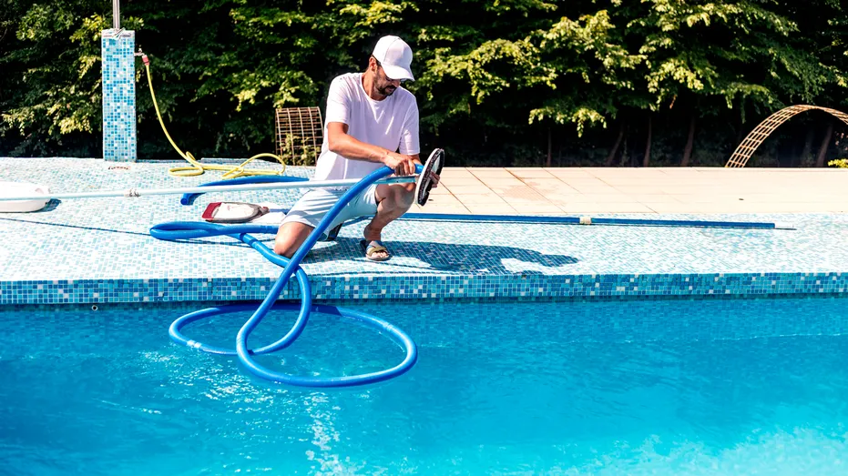 Un homme s’agenouille au bord d’une piscine avec du matériel.