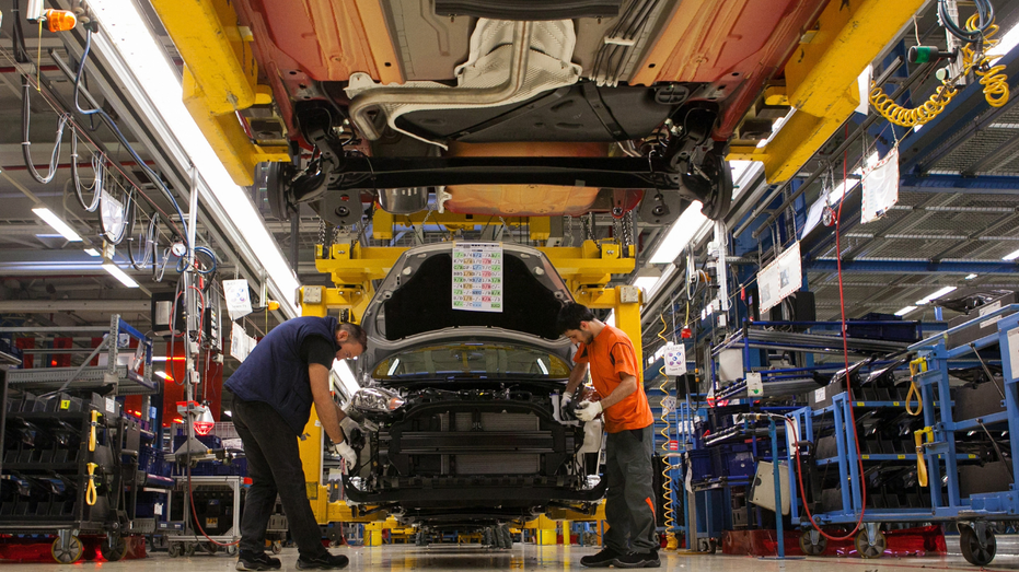 On voit des hommes travailler sur une voiture dans une usine Ford.