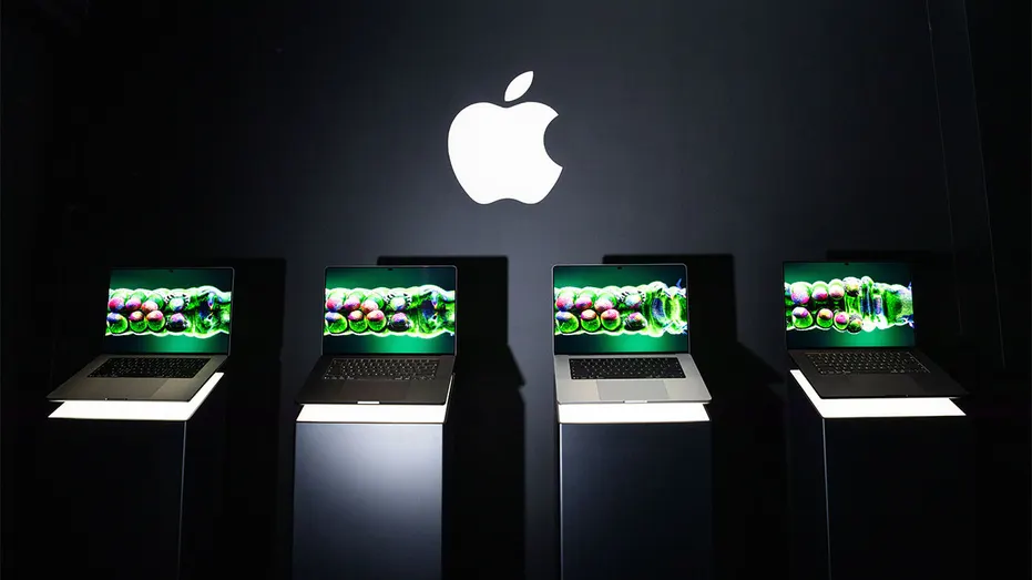 Quatre ordinateurs portables Apple MacBook Pro affichés sur des supports éclairés sous un grand logo Apple